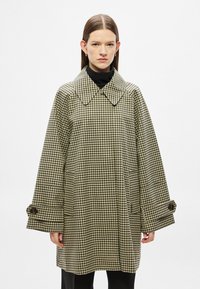 Manteau à motif pied-de-poule en noir et blanc, doté d'un large col, de manches larges et de poignets à boutons. Tissu texturé avec poches.