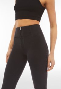 Pantaloni in denim neri a vita alta con zip frontale, caratterizzati da una texture liscia e un design attillato che esalta le gambe.