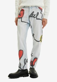 Ljusblå denimjeans med stora abstrakta mönster i rött, svart och gult. De har rak benform och bärs med svarta ankellångstövlar.