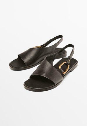 Sandales en cuir noir avec un bout ouvert et une sangle arrière, accentuées par une boucle dorée. Texture lisse avec un design de semelle plate.