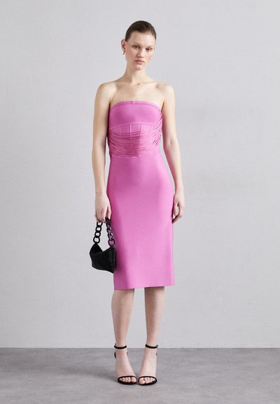 Strapless pink dress with gathered detailing at the bust, fitted silhouette, knee-length hem, paired with a black textured handbag and strappy heels.
