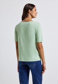 Un haut vert clair à manches courtes avec une coupe décontractée et un col rond. Texture douce, tissu lisse, affiché de dos. Associé à un jean bleu.