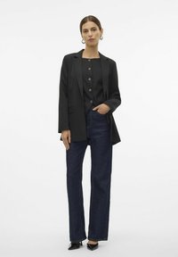 Black tailored blazer over a black buttoned top, paired with dark blue straight-leg jeans and black pointed-toe heels. Simple jewelry accents.