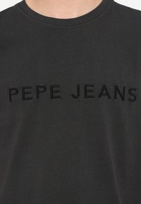 Mustast puuvillast t-särk, millel on tikandina musta värvi "PEPE JEANS" tekst. Klassikalise ümara kaelusega disain, lühikeste varrukatega ja siledapinnaline materjal.