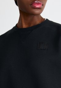 Sudadera negra con cuello redondo, que presenta un pequeño parche del logo negro de Jordan en la parte delantera, hecha de un material suave y texturizado.