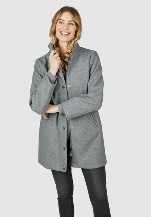 Manteau en laine grise avec un col montant, des boutons-pression et des poches latérales. Présente une texture lisse et une coupe décontractée, associé à un jean noir.
