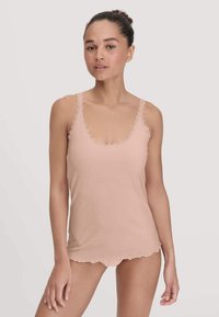 Woman wearing a light pink sleeveless camisole with lace trim and matching underwear, standing against a plain background.