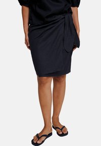 Mørkeblå omslagskjørt laget av lett stoff, med knytning i midjen og en glatt tekstur, kombinert med svarte flip-flops.