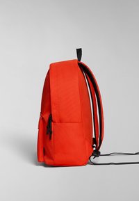 Mochila roja con un acabado textil suave, equipada con correas negras ajustables, un bolsillo lateral con cremallera y una forma rectangular compacta.