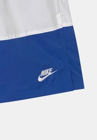 Pantalones cortos Nike en azul y blanco, con un tejido suave, costuras en contraste y un logo de Nike plateado en el borde inferior.