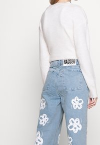 Maglione lavorato a maglia di colore chiaro con scollatura rotonda, abbinato a jeans azzurri chiari con motivi floreali bianchi sulle gambe e una vita con logo.