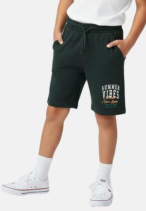 Groene katoenen shorts met een elastische tailleband, bedrukt met "SUMMER VIBES" in wit en oranje. Draagt witte sneakers en sokken.