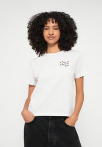 Λευκό βαμβακερό T-shirt με κοντά μανίκια, διακοσμημένο με κεντήματα λουλουδιών και τη λέξη "Hugo". Σχεδιασμένο με άνετη, κουτί εφαρμογή.