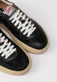 Sneaker nera in pelle lucida con lacci bianchi e suola in juta stile espadrilla. Presenta un logo sulla linguetta e dettagli perforati.