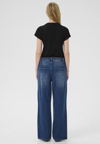 Čierna košeľa s krátkym rukávom a široké modré džínsové nohavice. Džínsy majú zadné vrecká a vysoký pás. Materiál je hladký s vyblednutým efektom.