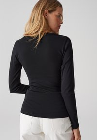 Schwarzes Langarmshirt mit taillierter Passform; glatte Textur. Hat einen runden Halsausschnitt und scheint aus dehnbarem Baumwollstoff gefertigt zu sein.