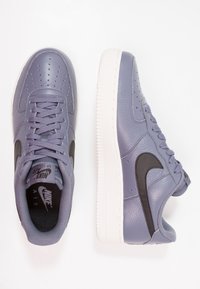Sneakers Nike Air Force 1 w lawendowej skórze z textured wykończeniem, czarną logo w kształcie zmarszczki i białą gumową podeszwą; posiada perforacje dla wentylacji.