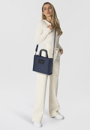 Sac à main en nylon bleu marine avec double poignée supérieure et une bandoulière amovible. Il présente une texture lisse et une forme rectangulaire.