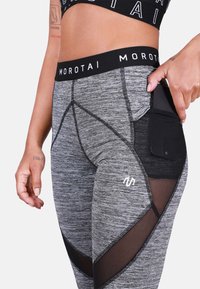 Szare legginsy sportowe z teksturowanej tkaniny, z czarną siateczkową kieszenią, kontrastowymi szwami oraz logotypem na udzie.