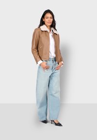 Bruine leren jas met een crèmekleurige bontkraag, rits aan de voorkant en zijzakken, gecombineerd met lichtblauwe wijde jeans en zwarte hakken.