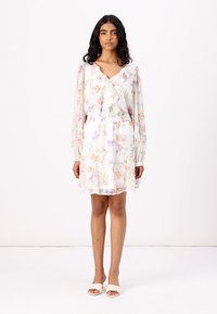 Robe florale en tissu transparent blanc, avec un col volanté, des manches longues, une taille élastique et des motifs de fleurs pastel en rose, violet et orange.