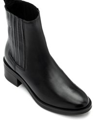 Botte de cheville en cuir noir avec des panneaux élastiques sur les côtés, talon bas et bout rond, présentée sur un fond blanc.