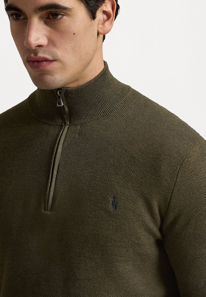 Maglione verde con zip, colletto a coste, trama testurizzata e logo in evidenza sul petto. Presenta una cerniera a metà lunghezza.