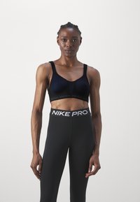 Svart sports-bh med mesh-paneler og brede stropper, kombinert med høyhånds svart leggings med en hvit "Nike Pro" livlinje.