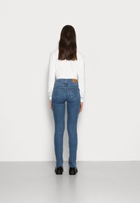 Jeans skinny de ganga azul com cintura média, apresentando um retalho de couro castanho na parte de trás e estilo tradicional de cinco bolsos.