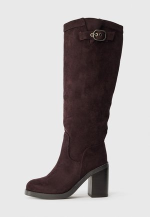 Botas de ante burdeos hasta la rodilla con tacón cuadrado, acentuadas por un detalle de hebilla lateral y una superficie lisa y texturizada.