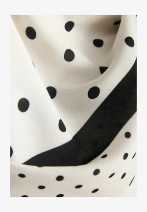 Czarne kropki na kremowej tkaninie o gładkiej fakturze, z kontrastującym czarnym pasem wzdłuż krawędzi tkaniny.