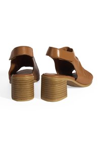 Braune Leder-Absatzsandalen mit Ausschnitten und einem gestapelten Absatz. Die vertikalen Rillen des Absatzes sorgen für Textur. Verstellbarer Riemen für sicheren Halt.