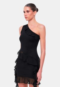 Schwarzes-Minikleid ohne Ärmel mit einem Schulterträger und Rüschendetails. Hergestellt aus glattem Stoff mit transparenten Rüschen am Saum und an der Seite.