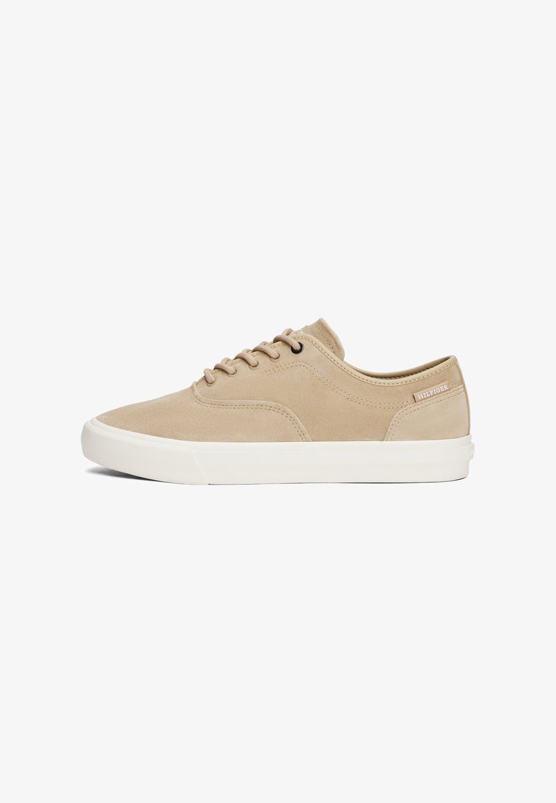 Baskets basses en daim beige avec semelle en caoutchouc blanc et lacets beiges, étiquette latérale avec le nom de la marque, vues de l'extérieur.
