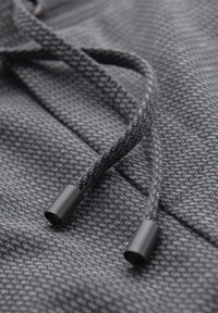 Nahaufnahme eines grauen Strickstoffes mit geflochtenen Kordeln, die in schwarzen Kunststoffenden münden.