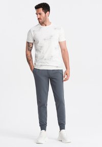 Hvid t-shirt med et spredt, gråt dottet mønster, der er parret med grå joggers og hvide sneakers, som fremhæver en afslappet pasform og blødt stof.