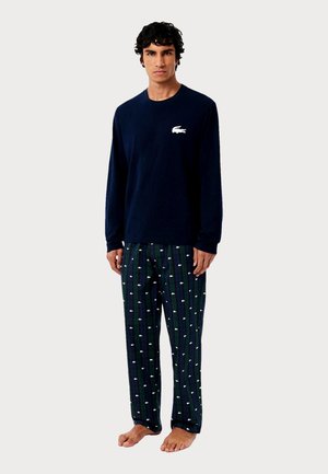 Marineblaues Langarmhemd mit weißem Logo; gemusterte Schlafanzughose mit grünen Streifen und kleinen weißen Logos; Baumwollmaterial, lockere Passform.