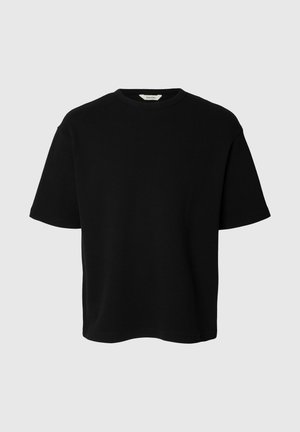 T-shirt noir à manches courtes et col rond avec une coupe décontractée et une texture de tissu visible sur un fond gris clair.