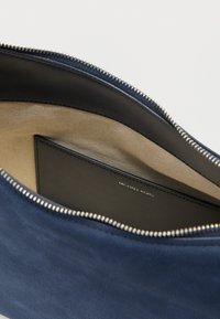 Εσωτερικό της μπλε δερμάτινης τσάντας με μπεζ ύφασμα επένδυσης, διαθέτοντας φερμουάρ κλεισίματος και μαύρο θήκη καρτών με ανάγλυφο το «MICHAEL KORS».