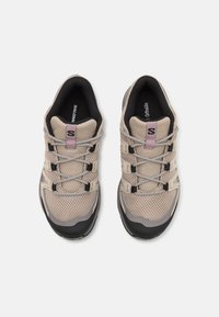 Chaussures d'extérieur en maille beige avec des accents gris, dotées de lacets élastiques et d'une semelle en caoutchouc noir robuste. Surface texturée et design respirant.