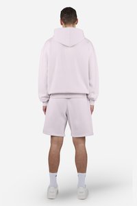 Sudadera rosa claro con capucha, combinada con pantalones cortos a juego. Tela suave, corte relajado, con puños y cinturilla acanalados. Estilizada con zapatillas blancas.