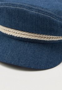 Denim cap featuring a deep blue color, rounded shape, and a contrasting cream rope accent along the rim.