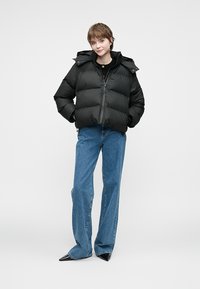 Jachetă puffer neagră cu glugă, design matlasat și fermoar frontal. Asortată cu blugi blue cu talie înaltă și pantofi negri cu vârf ascuțit.