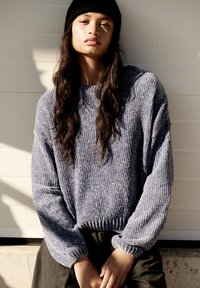 Pull en maille épaisse de couleur lavande douce, avec une texture côtelée, des manches larges et un bas ajusté. Associé à un pantalon sombre et un bonnet noir.