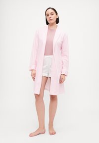 Lyserosa stripete badekåpe med lange ermer, åpen front og to lommer, brukt over en rosa topp og hvite shorts. Glatt, lett stoff.