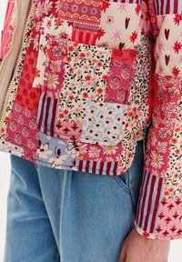 Zateplená bunda s patchworkovým dizajnom, na ktorej sú kvetinové a prúžkované vzory v odtieňoch ružovej, červenej, modrej a bielej. Obsahuje predné vrecko.