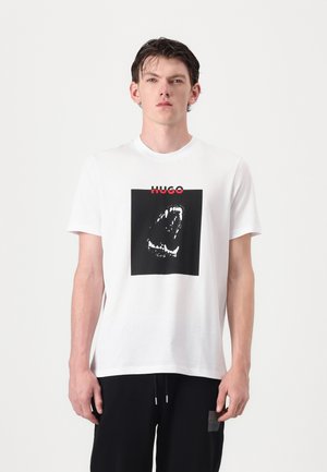 Weißes Baumwoll-T-Shirt mit einem schwarzen quadratischen Grafik eines Mundes mit Zähnen und dem Markennamen "HUGO" in Rot darüber.