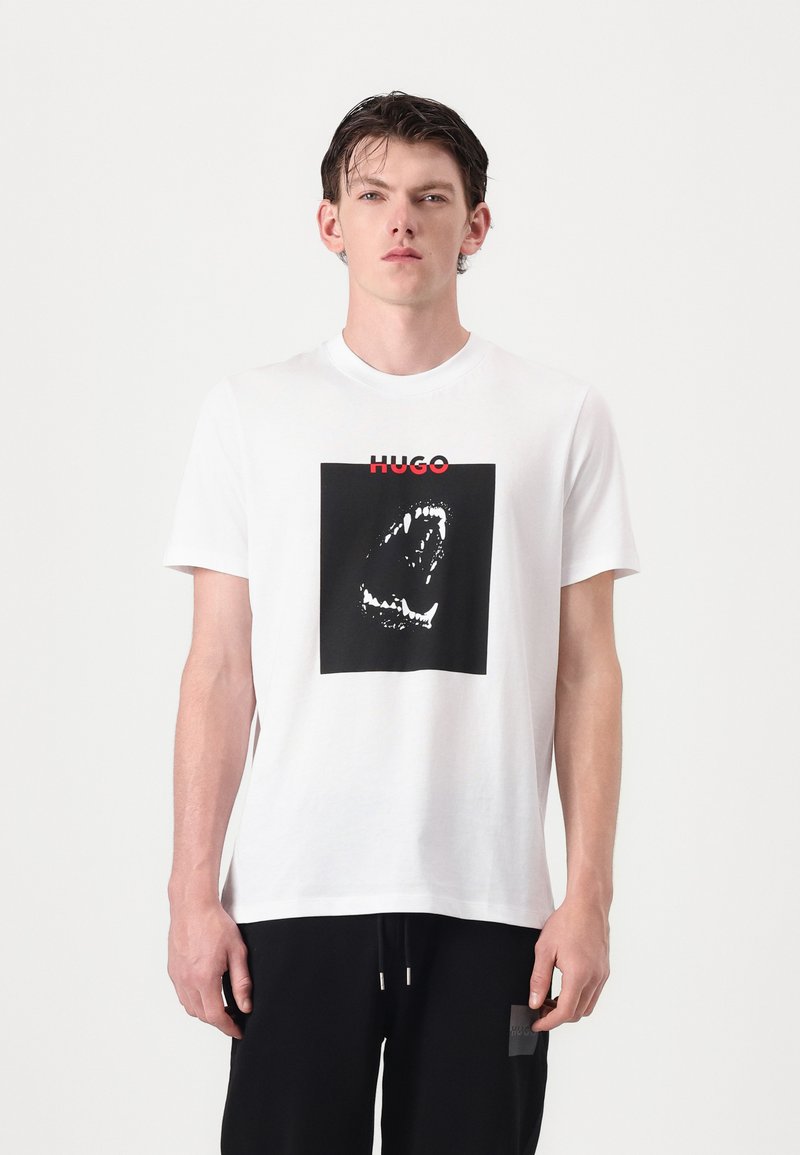 Hvit bomull t-skjorte med et svart kvadratisk grafikk av en munn med tenner, og merkets navn "HUGO" i rødt over.