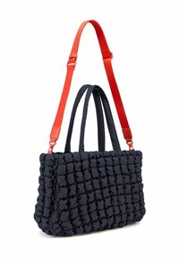 Sac en bandoulière matelassé bleu marine avec une sangle et des poignées ajustables orange. Surface texturée avec des bulles rembourrées, offrant un design visuel distinct.