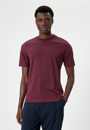 Burgunderfarbiges Baumwoll-T-Shirt mit kurzen Ärmeln, Rundhalsausschnitt, einfarbig, glatte Textur und einem schlichten Design. Getragen mit marineblauen Hosen.